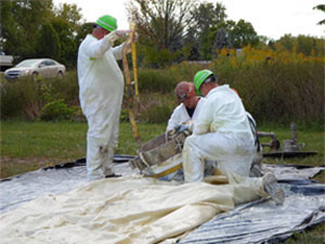 Three construction workers outside kneeling on tarp